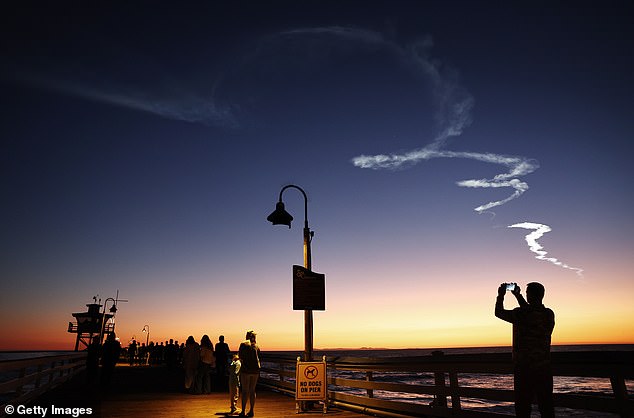 Menschen laufen auf einem Pier unter dem Kondensstreifen einer SpaceX Falcon 9-Rakete in San Clemente
