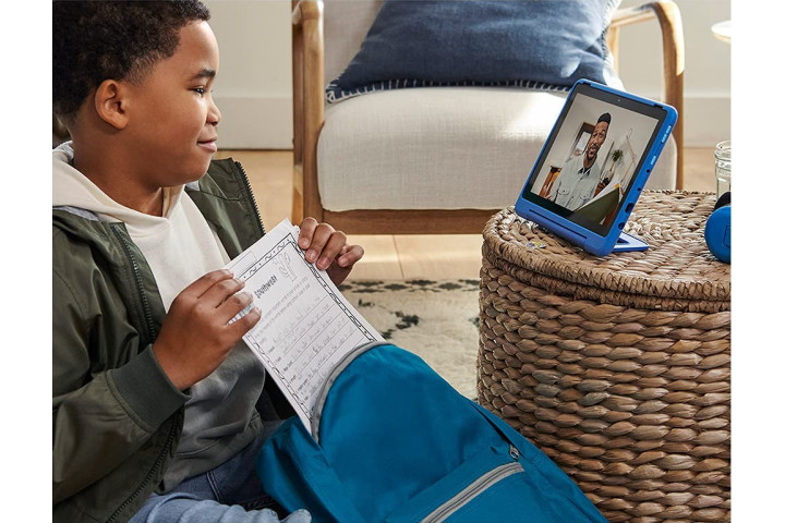 Ein Junge mit einem Arbeitsblatt, der sich ein Video auf einem blauen Amazon Fire HD 10 Kids Pro ansieht.