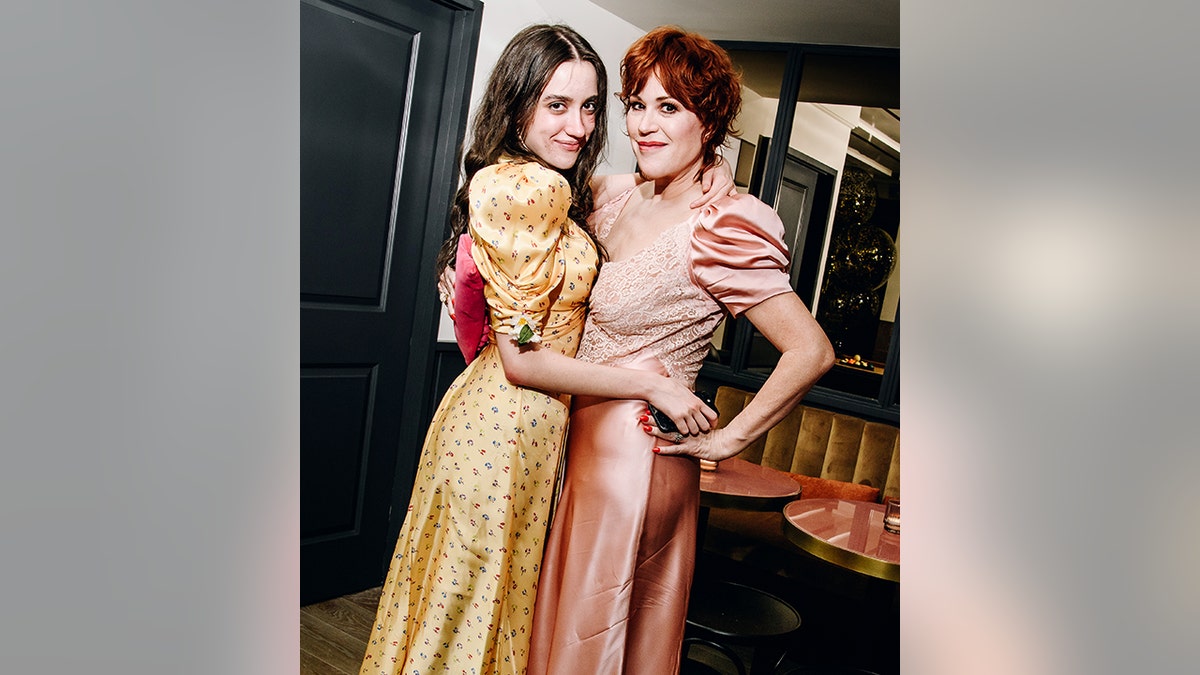 Molly Ringwald in einem hellrosa Kleid mit Puffärmeln legt ihren Arm um Tochter Mathilda in einem gelben Kleid mit Puffärmeln