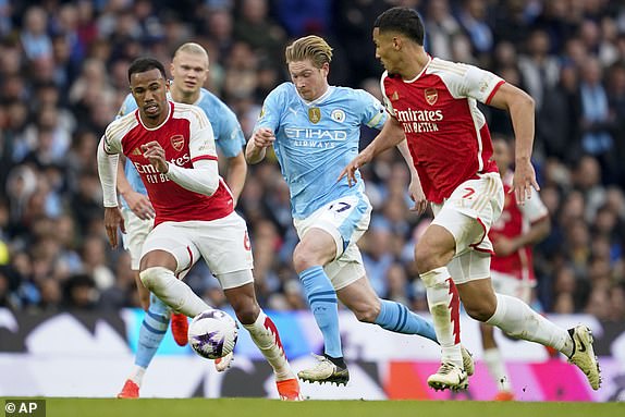 Manchester City's Kevin De Bruyne, center, duels for the ball with Arsenal's Gabriel, left, and Arsenal's William Saliba during the English Premier League soccer match between Manchester City and Arsenal at the Etihad stadium in Manchester, England, Sunday, March 31, 2024. (AP Photo/Dave Thompson)