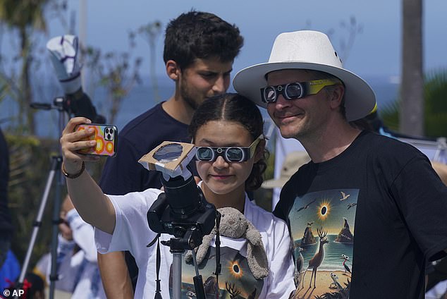 Menschen machen Selfies, während sie am Montag, den 8. April 2024, in Mazatlan, Mexiko, eine totale Sonnenfinsternis beobachten und fotografieren. Sie haben einen Filter an ihrer Kamera angebracht, der auf den Himmel gerichtet ist.