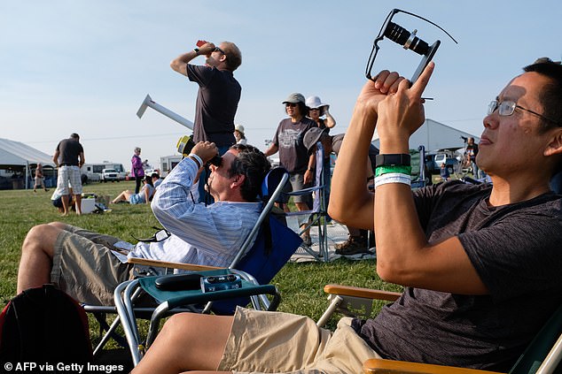 Amos Yew (R) verwendet ein Objektiv eines iPhones mit schützender Sonnenbrille über dem Objektiv, um Videos in den ersten Phasen der totalen Sonnenfinsternis am 21. August 2017 in Madras, Oregon, aufzunehmen.
