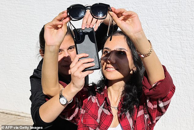 Frauen betrachten am 25. Oktober 2022 in Ankara eine partielle Sonnenfinsternis mit Sonnenbrille durch eine Smartphone-Kamera.