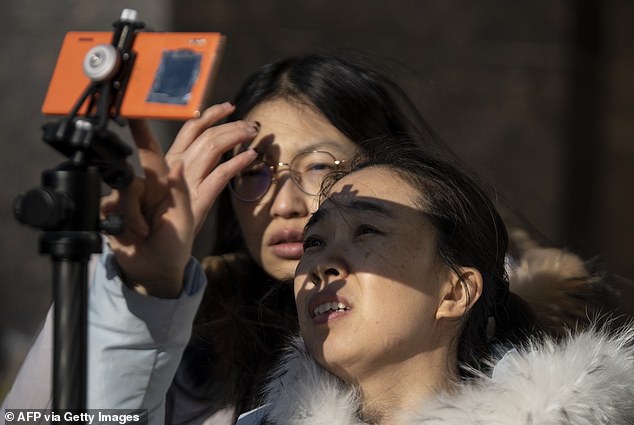 Menschen nutzen ein Smartphone, um etwas Seltenes anzusehen "Feuerring" Sonnenfinsternis in Peking am 26. Dezember 2019. Zu sehen ist ein Filter, der das Objektiv der Telefonkamera abdeckt.