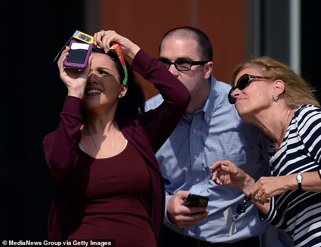 Kayla Ketz (links) fotografiert mit einer Sonnenfinsternisbrille die Sonnenfinsternis mit einem Smartphone, während ihre Kollegen Joe Belovich und Nancy Dyer am Montag, dem 21. August 2017, im Bostoner Seaport District zuschauen.