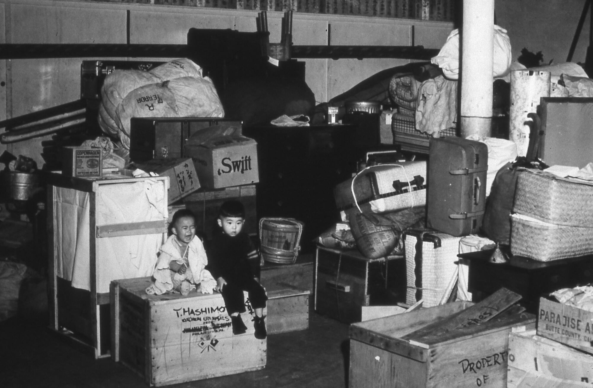Ein weinendes Mädchen und ein Junge sitzen zwischen den Kisten und Koffern von Menschen japanischer Abstammung, die 1942 inhaftiert wurden. 