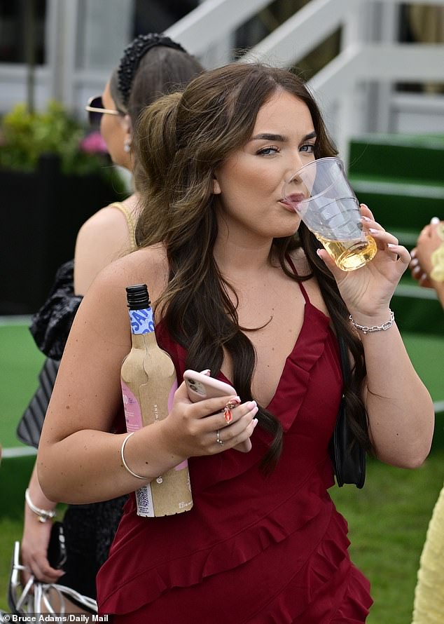 One woman is pictured taking a sip of her drink at Aintree today