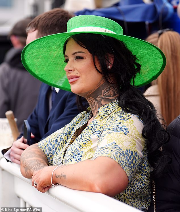 One woman wearing a green wide-brimmed hat looks out onto the race course