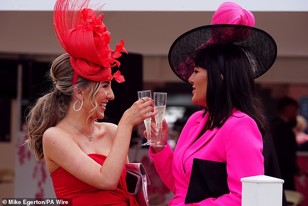 Cheers! Two racegoers are pictured clinking their champagne glasses together as revellers kick of Aintree day two