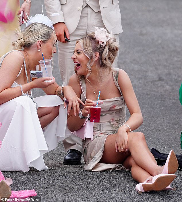 Two women are snapped having a laugh while holding their drinks as they sit down on the floor