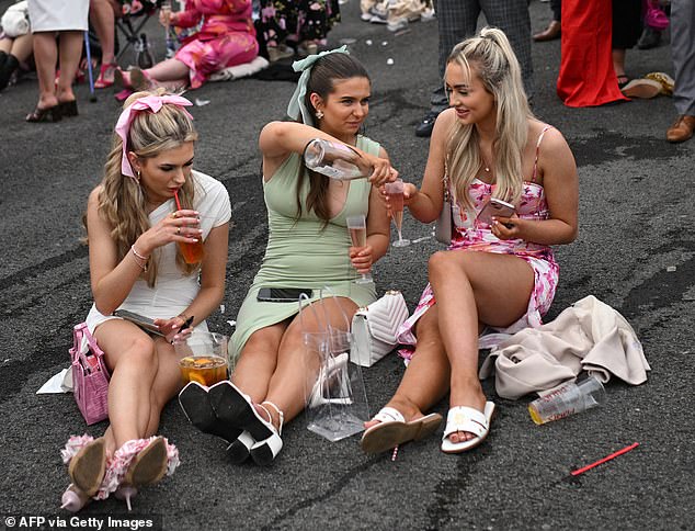 Three women pour wine as they sit on the floor of Aintree on the event's second day