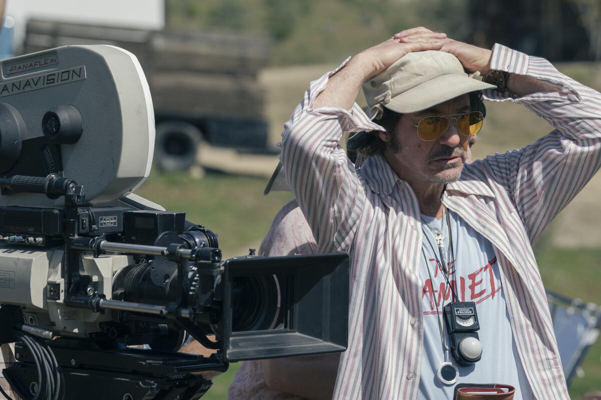 Ein Mann mit den Händen auf dem Kopf steht neben einer Filmkamera.
