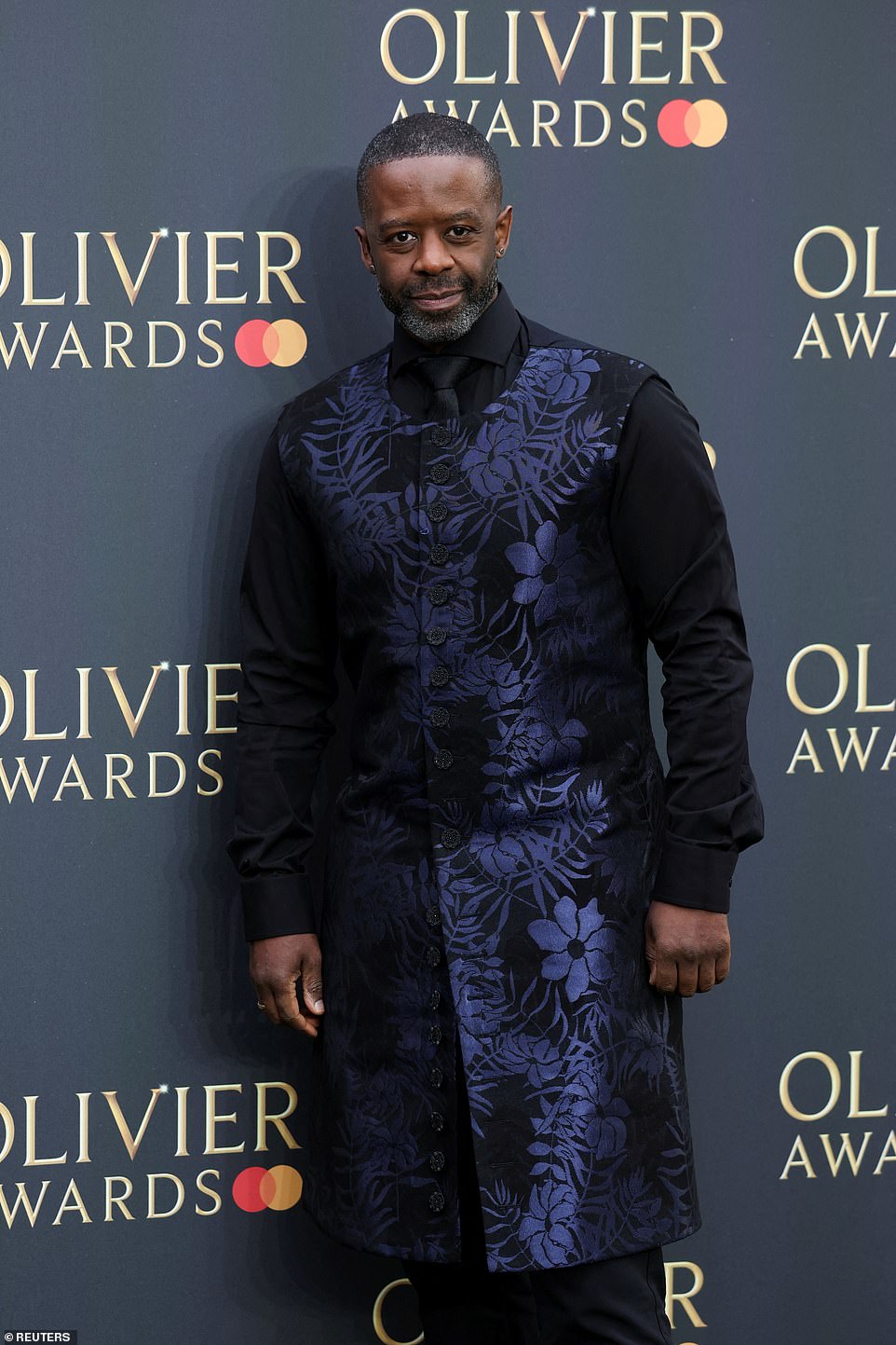 Adrian Lester looked sharp in a black shirt and tie, with a button down tunic layered over the top, embroidered in a blue floral design