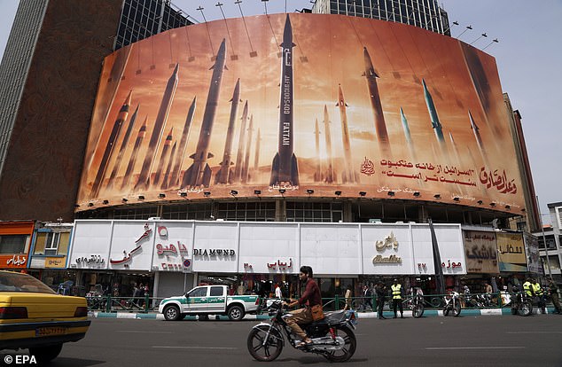 Iraner fahren am 16. April 2024 in Teheran an einer riesigen Anti-Israel-Werbetafel mit Bildern iranischer Raketen und einem persischen Satz mit der Aufschrift „Israel ist schwächer als Spinnenheim“ vorbei