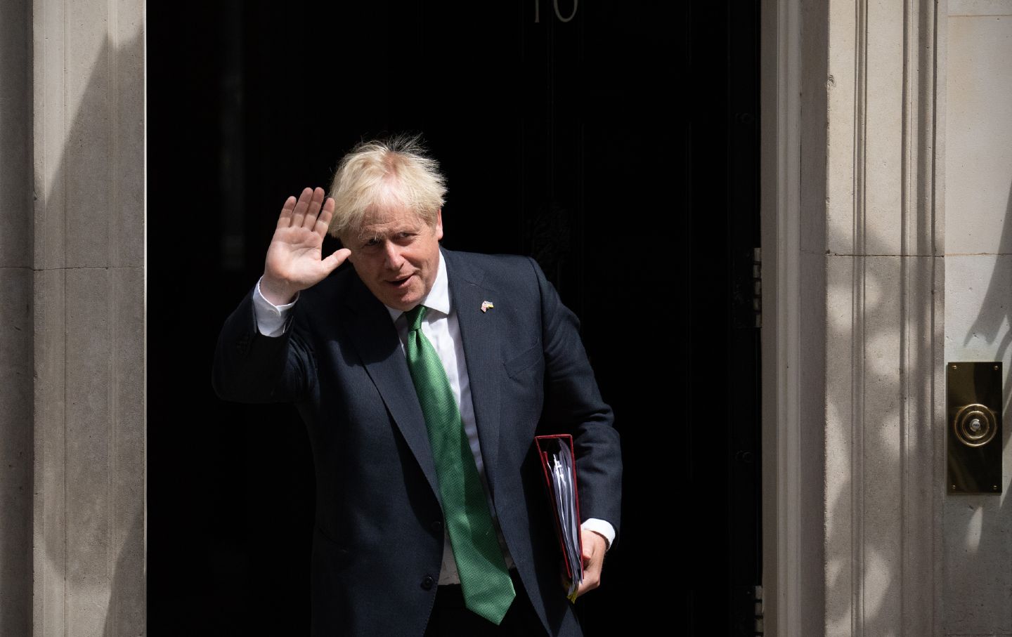 Der scheidende britische Premierminister Boris John winkt, als er 10 Downing Street verlässt, um an den Fragen des Premierministers teilzunehmen.  Er hält einen Ordner in der Hand und trägt einen Anzug mit grüner Krawatte.
