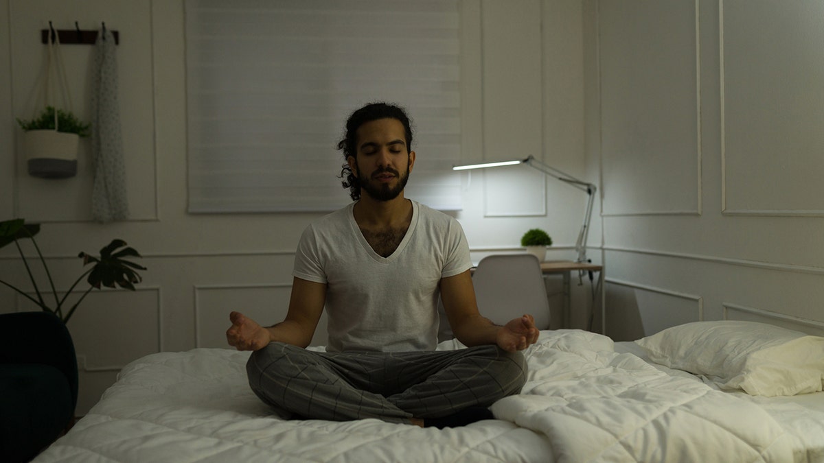 Mann meditiert nachts auf seinem Bett