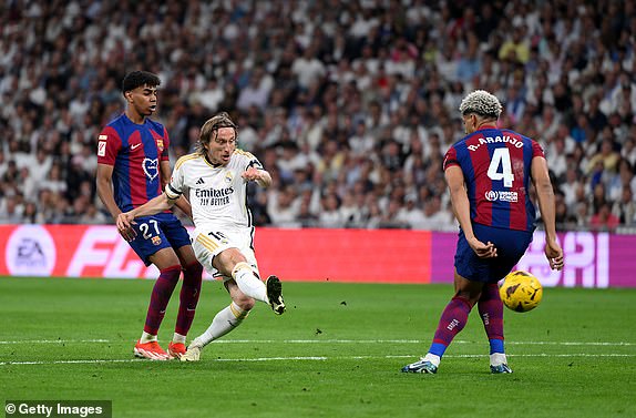 MADRID, SPAIN - APRIL 21: Luka Modric of Real Madrid takes a shot whilst under pressure from Lamine Yamal and Ronald Araujo of FC Barcelona during the LaLiga EA Sports match between Real Madrid CF and FC Barcelona at Estadio Santiago Bernabeu on April 21, 2024 in Madrid, Spain. (Photo by David Ramos/Getty Images)