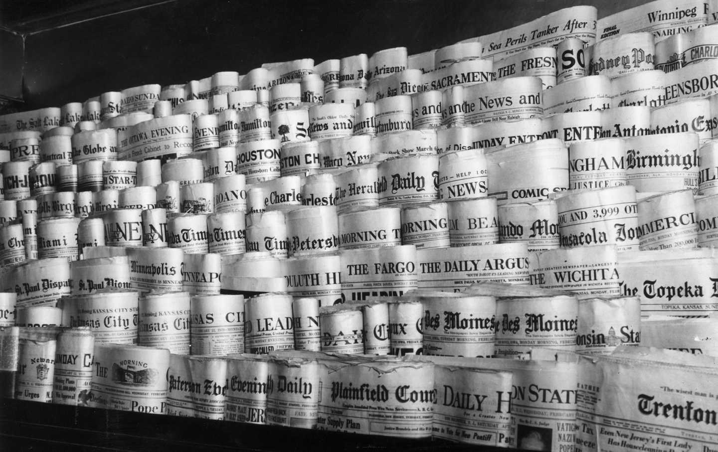 Eine Ausstellung von Dutzenden Lokalzeitungen zum Verkauf an einem Zeitungskiosk auf einem Schwarzweißfoto.