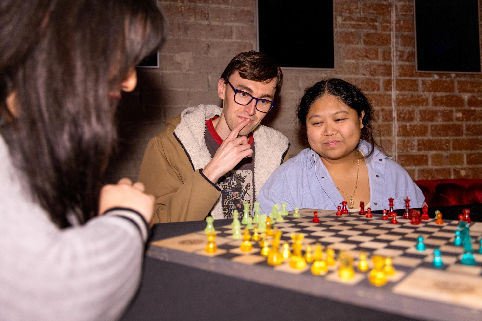 Drei Personen spielen gemeinsam Schach auf einem Mehrspielerbrett.