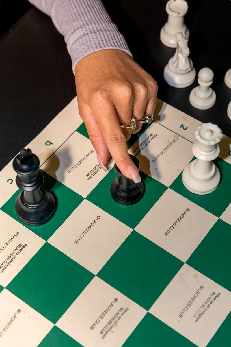 Eine Nahaufnahme einer Hand, die eine Schachfigur auf einem grünen Schachbrett bewegt.