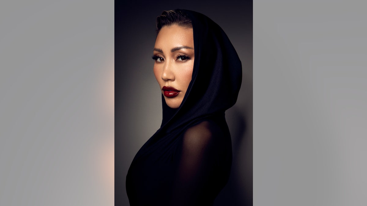Aliia Roza blickt in einem transparenten schwarzen Kleid mit Kapuze zur Seite
