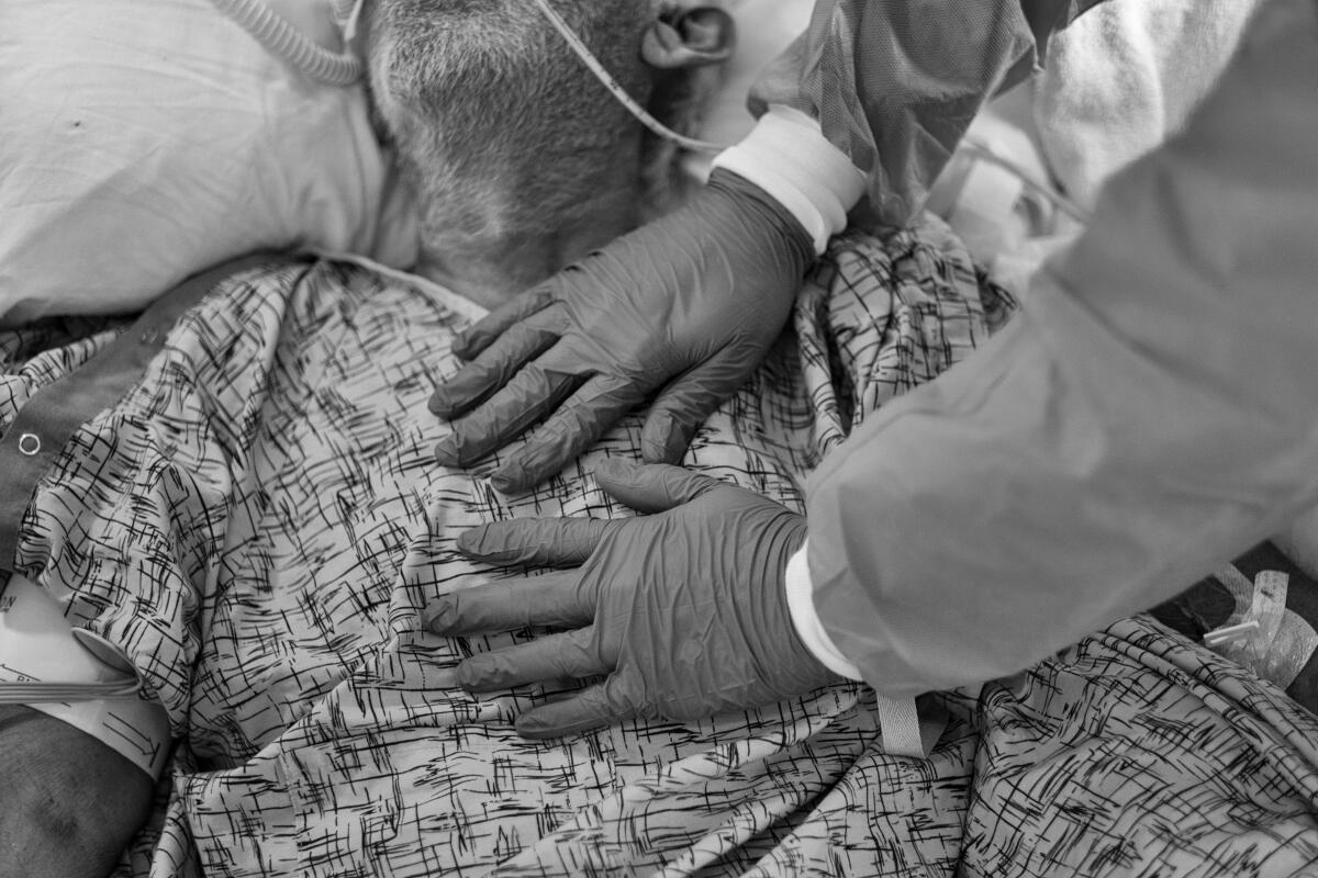Die behandschuhten Hände eines Seelsorgers schweben über dem Herzen eines COVID-19-Patienten mit Sauerstoffschläuchen in der Nase.