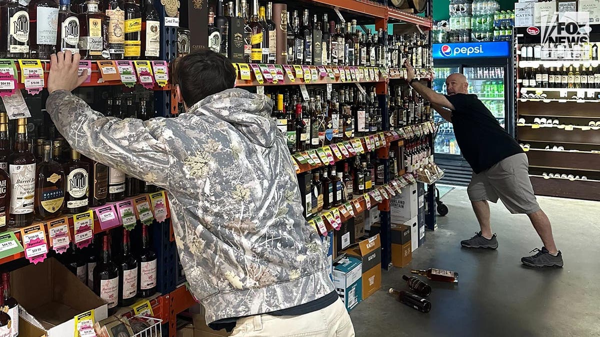 Zwei Männer halten ein Regal mit Spirituosenflaschen davon ab, zu wackeln