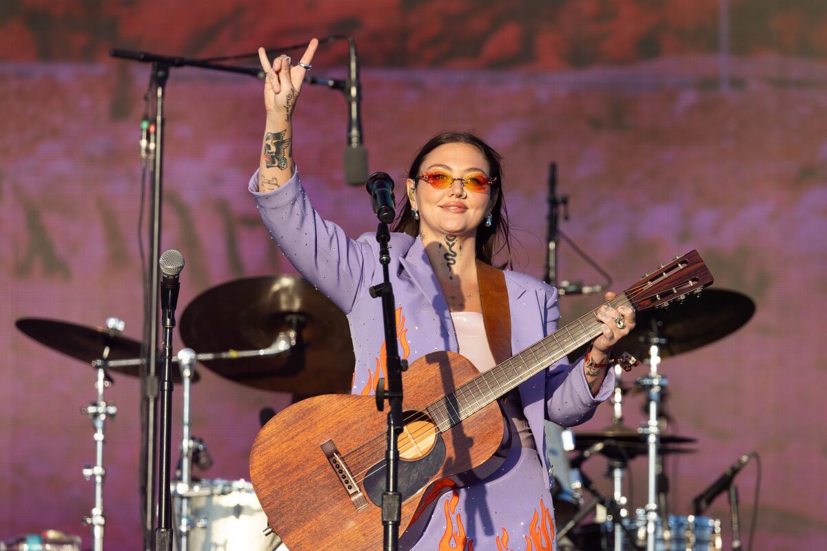 Eine Gitarristin hebt während ihres Auftritts ihre rechte Hand zum Symbol der Rockhörner.