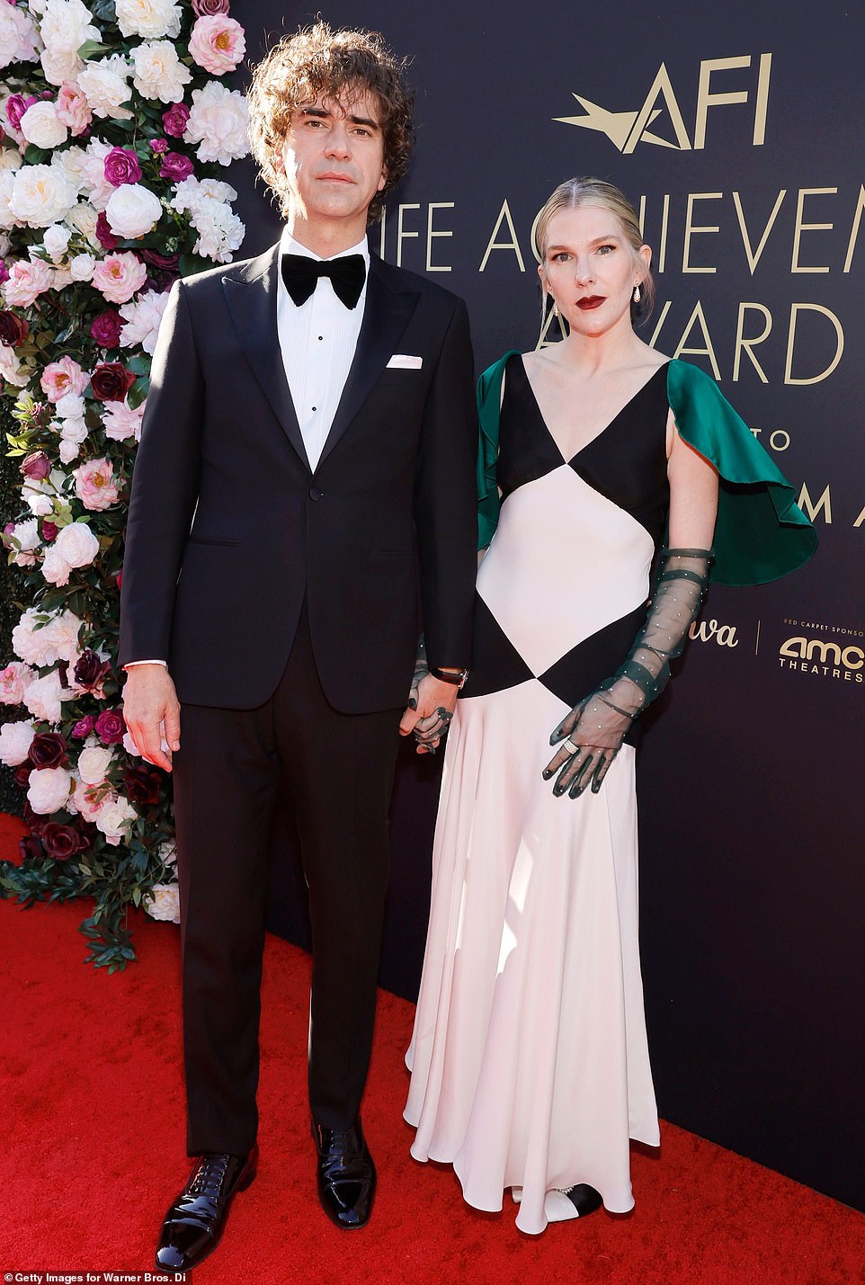 Lily Rabe channeled old glamour in a white ankle-length dress with black diamond cutouts and a short green satin cape as she arrived with husband Hamish Linklater