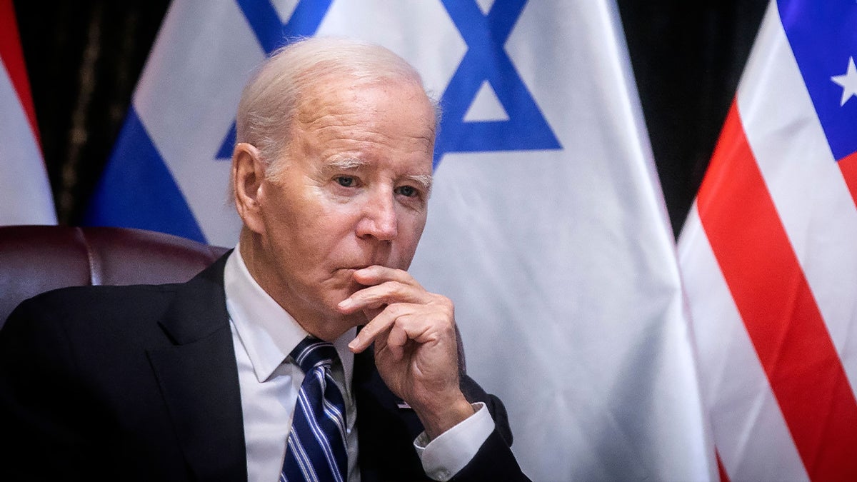 Biden sitzt mit der Hand an den Lippen vor der israelischen Flagge