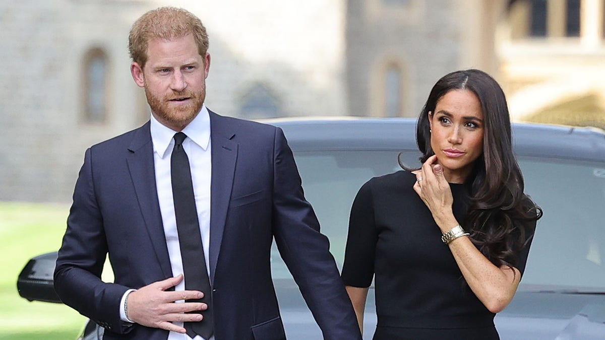 Prinz Harry in einem dunkelblauen Anzug und einer Krawatte hält Meghan Markles Hand und trägt ein dunkles Kleid, nachdem die Königin gestorben ist