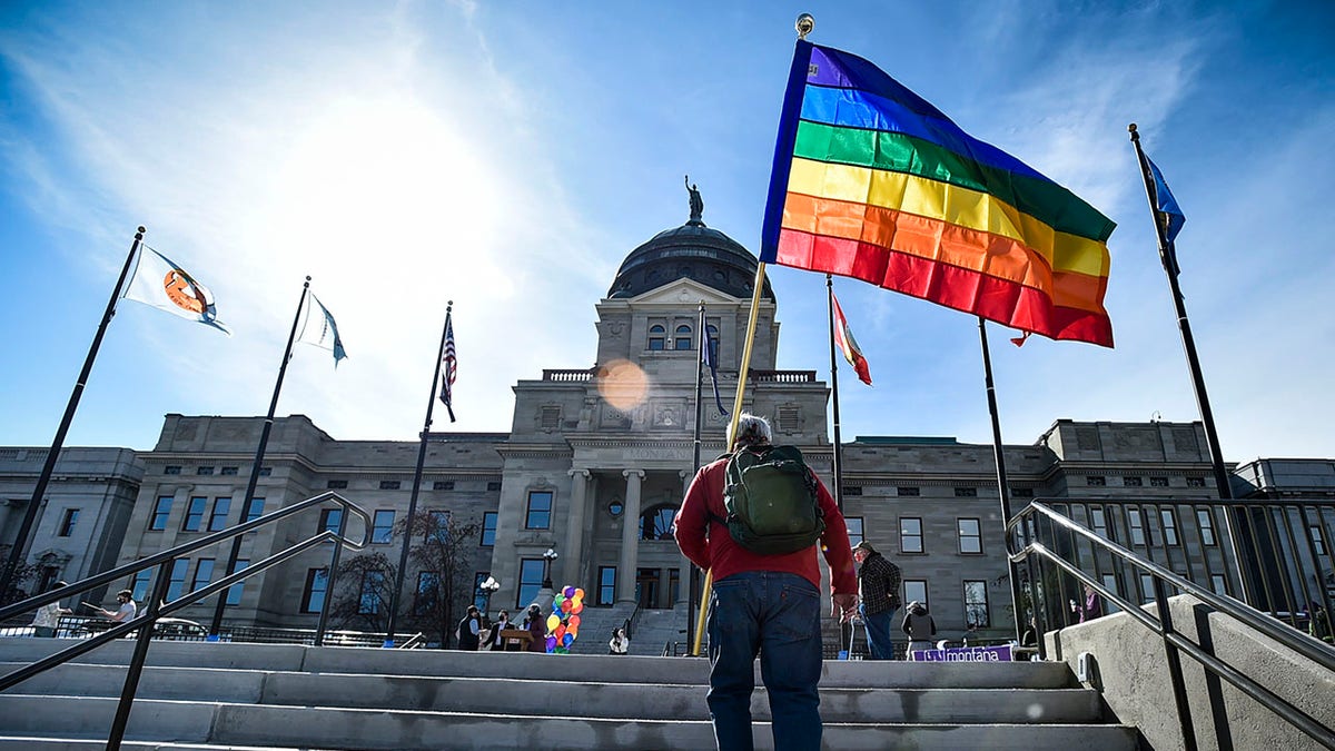 Mann trägt Regenbogenfahne die Treppe vor der Hauptstadt des Bundesstaates Kansas hinauf
