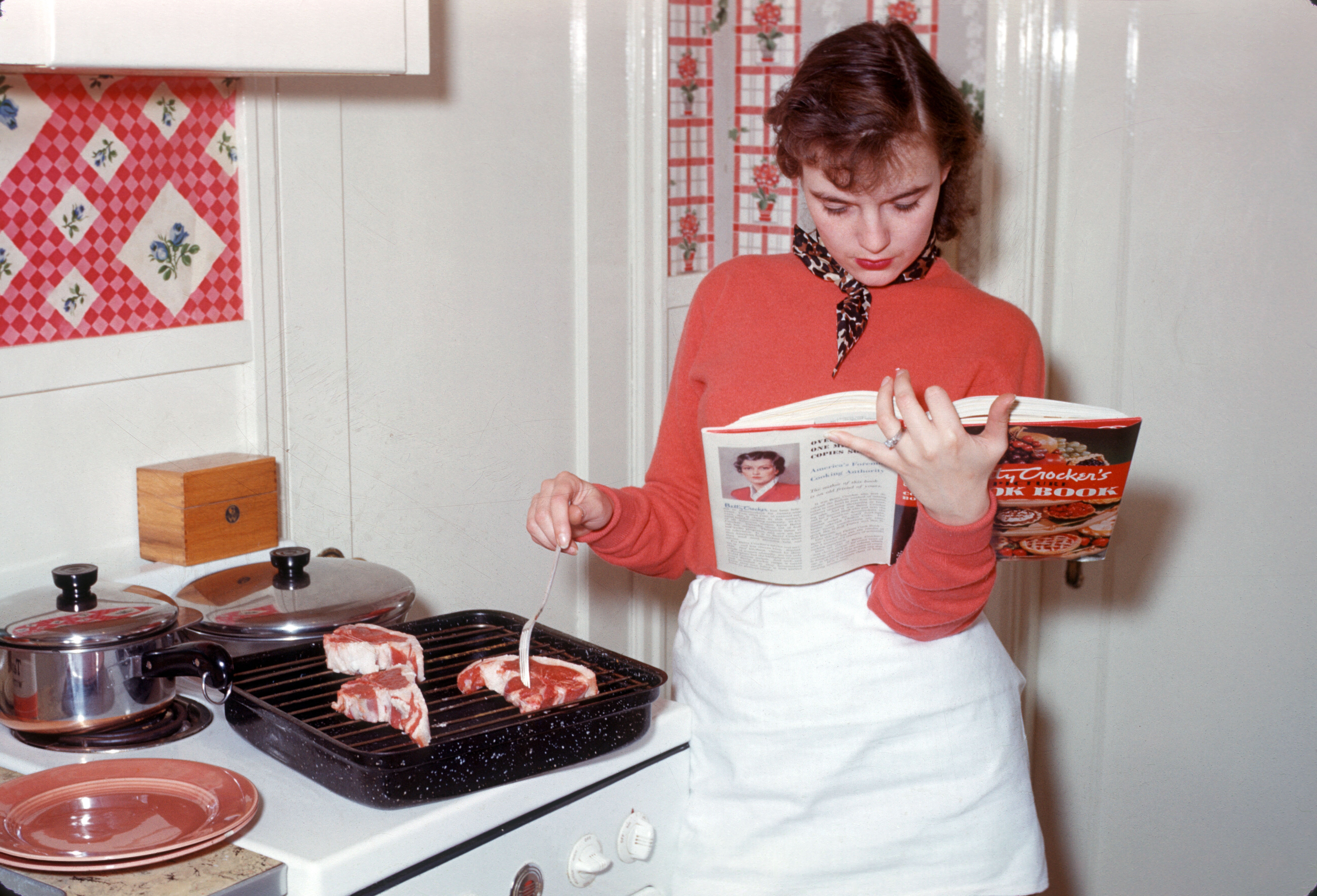 Ein Vintage-Foto einer Frau, die einen Topf rührt, während sie ein Kochbuch liest