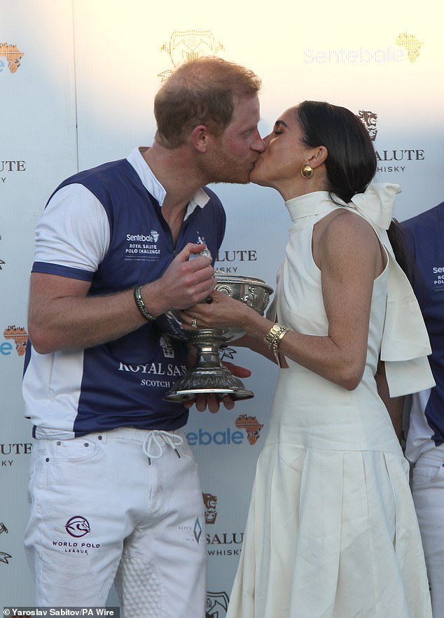 The Duchess of Sussex presents the trophy to her husband, the Duke of Sussex after his team the Royal Salute Sentebale Team