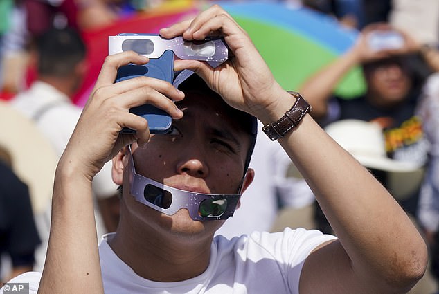 Ein Mann fotografiert am Montag, den 8. April 2024, eine totale Sonnenfinsternis in Mazatlan, Mexiko. Er trägt eine Sonnenfinsternisbrille, um seine Kamera und seine Augen zu schützen.