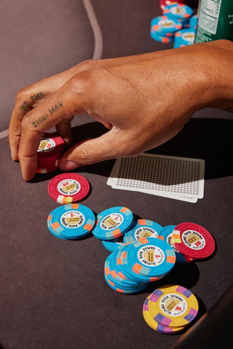 Auf einem Tisch verstreute Pokerchips, eine Hand schwebt über ein paar roten Chips. 