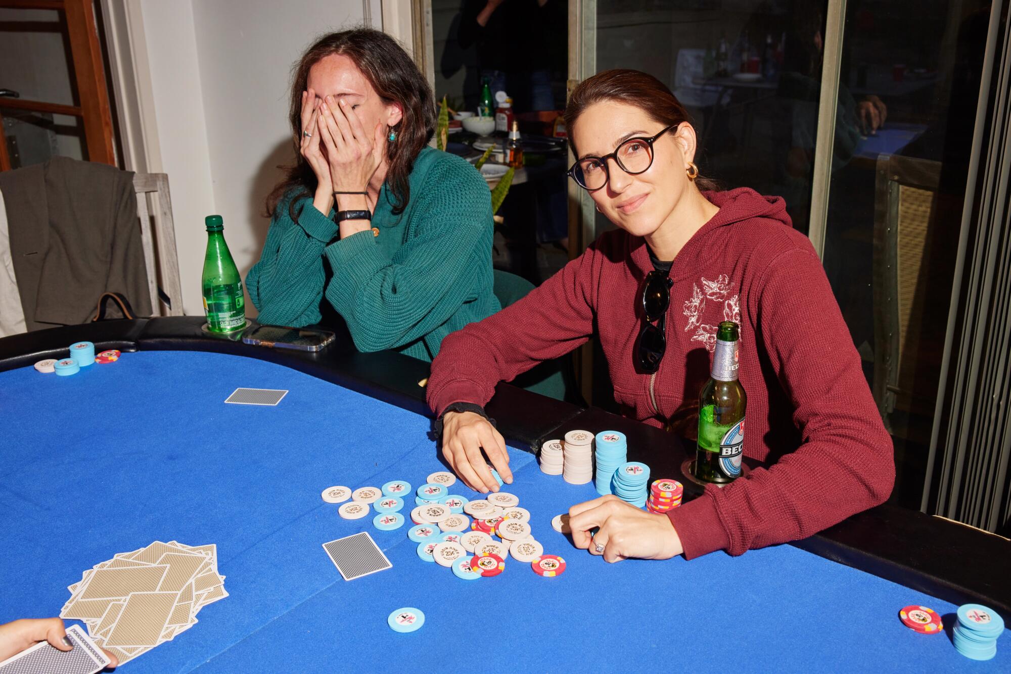 Zwei Frauen sitzen an einem Pokertisch, eine bedeckt ihr Gesicht, die andere scheffelt die Chips