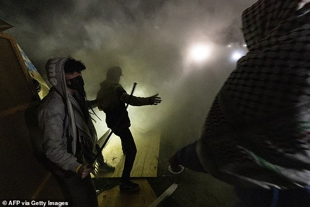 Pro-Palestinian demonstrators engulfed in tear gas regroup and rebuild the barricade surrounding the encampment set up on the campus of UCLA