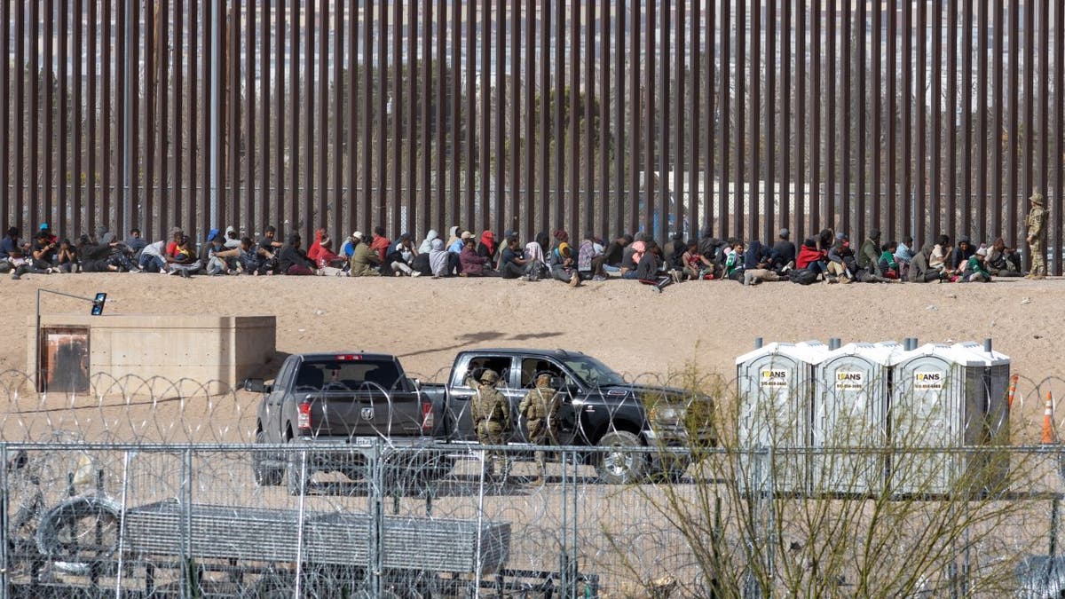 Migranten sitzen in der Nähe der Grenzmauer