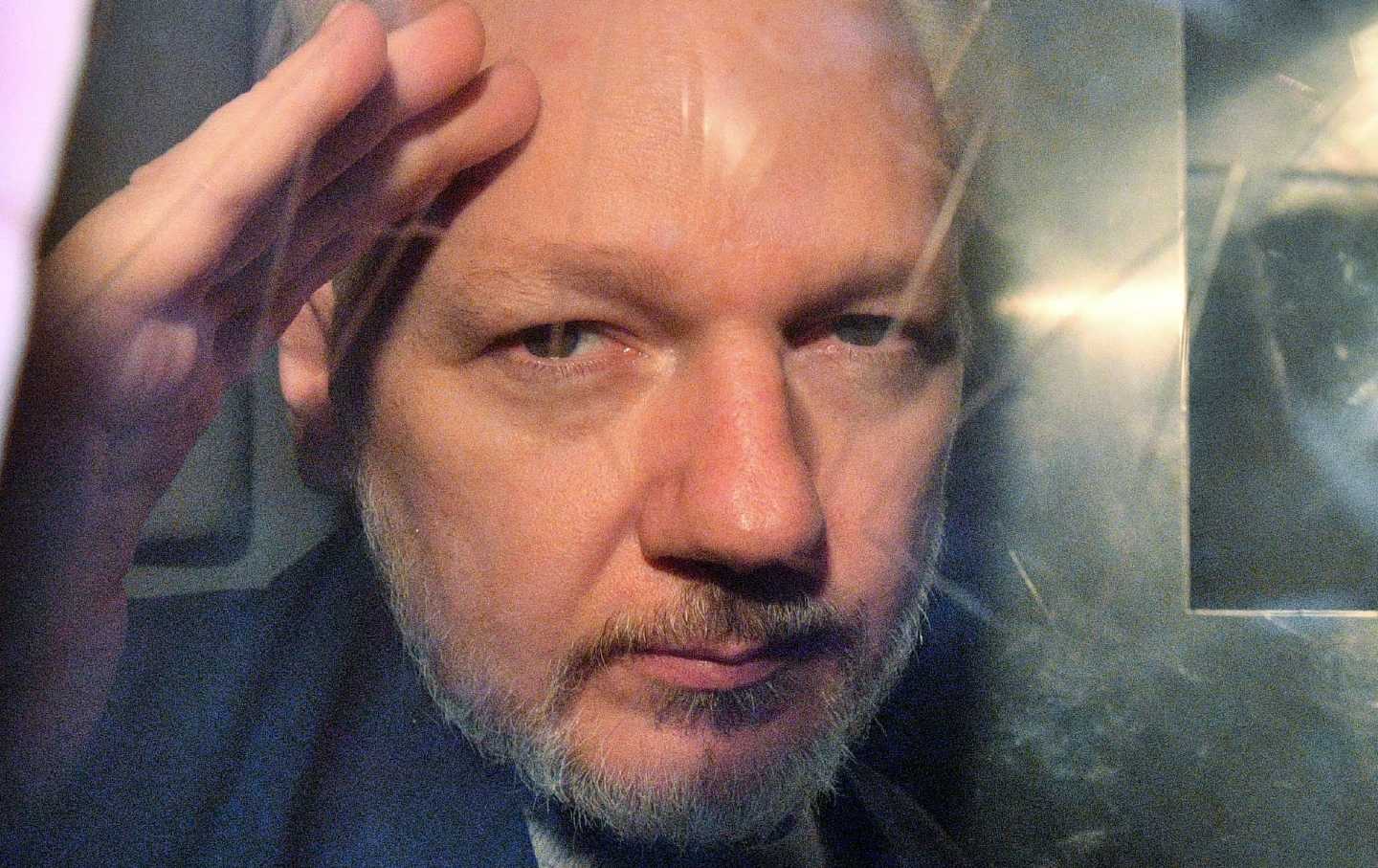 Julian Assange winkt leicht und hält sein Gesicht dicht an der Scheibe eines Gefängnistransporters