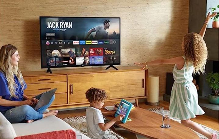 Eine Familie spielt in einem Wohnzimmer mit einem Amazon Fire TV an der Wand.
