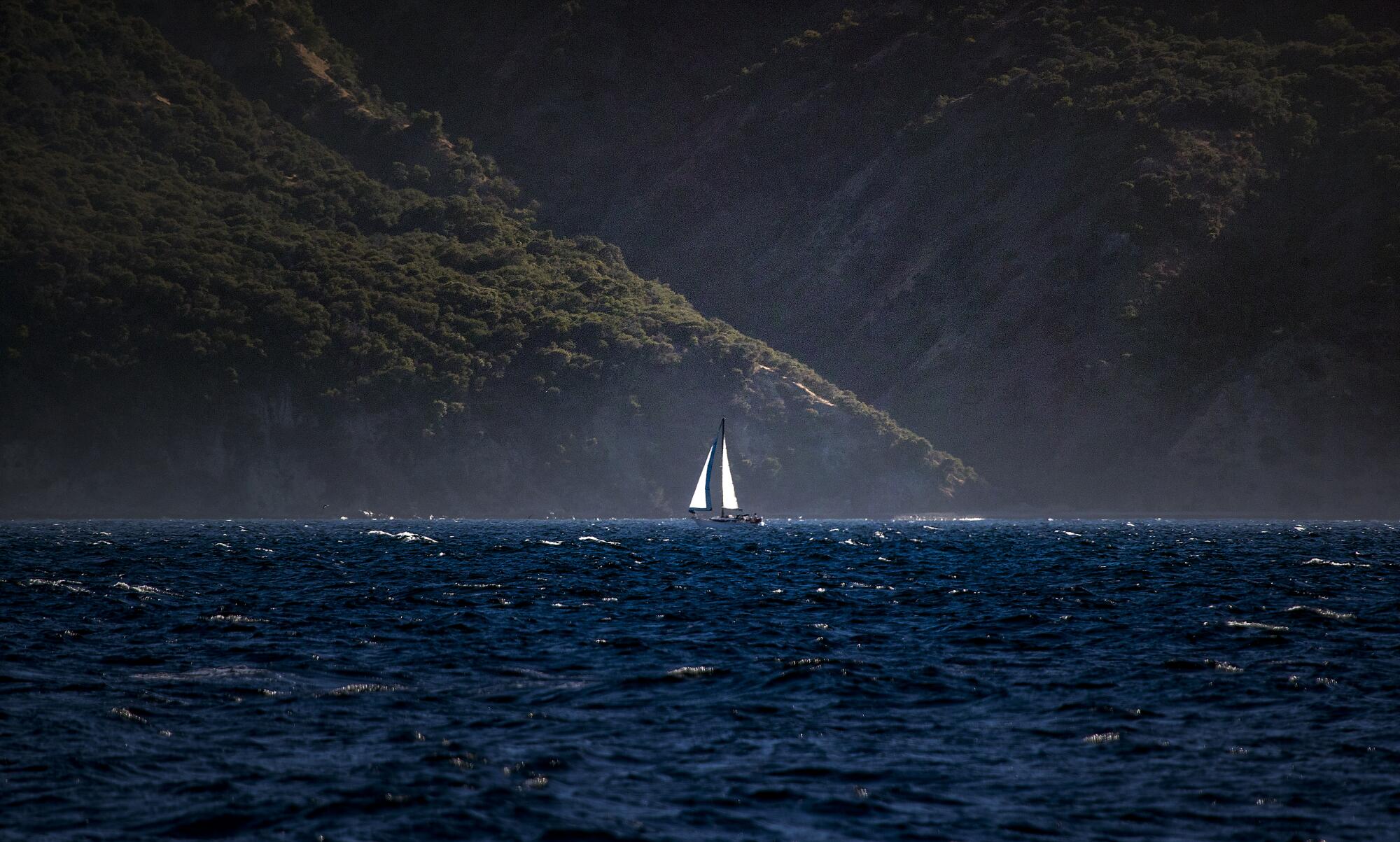Hinter einem einsamen Segelboot erheben sich Berge auf einer Insel.