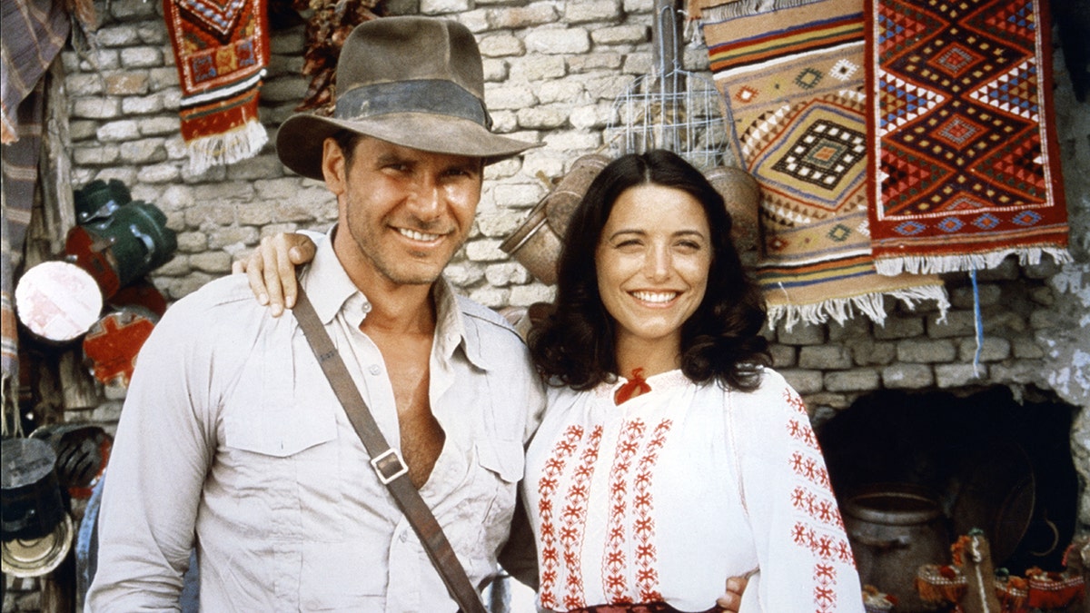 Harrison Ford in einem weißen Hemd lächelt neben Karen Allen in einer weißen Bluse "Indiana Jones" Satz