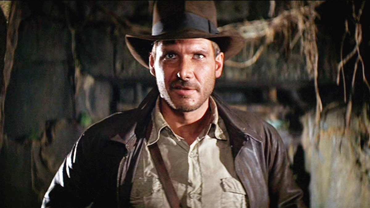 Harrison Ford trägt eine braune Lederjacke und einen braunen Hut "Indiana Jones"