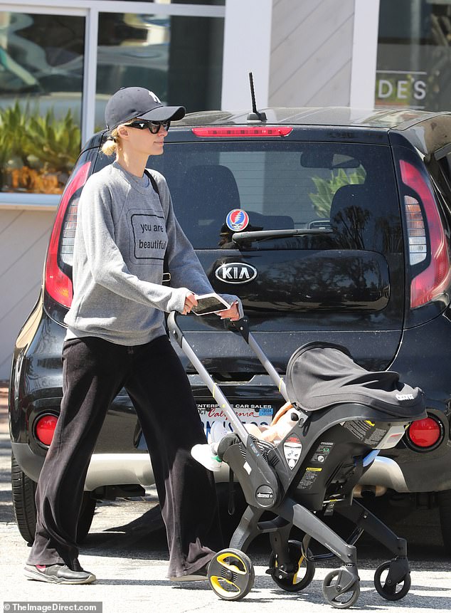 Sie trug ein graues Sweatshirt und eine schwarze Jogginghose, während sie ihr Baby auf dem Arm trug