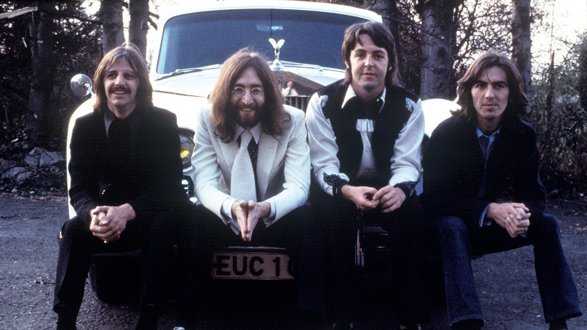 Die Beatles posieren gemeinsam auf der Stoßstange eines Autos