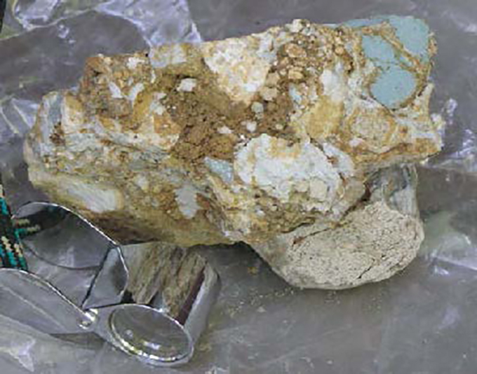 A photograph of a brown, white and turquoise-blue rock from Yellowstone Lake that shows signs of being altered by hot water