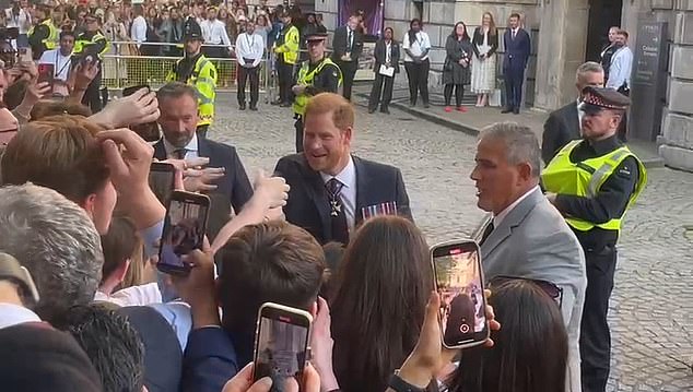 Der Herzog scherzte mit einem begeisterten Royal-Fan, der mit zwei Telefonen die Arme ausgestreckt hatte, um das beste Foto von Harry zu machen