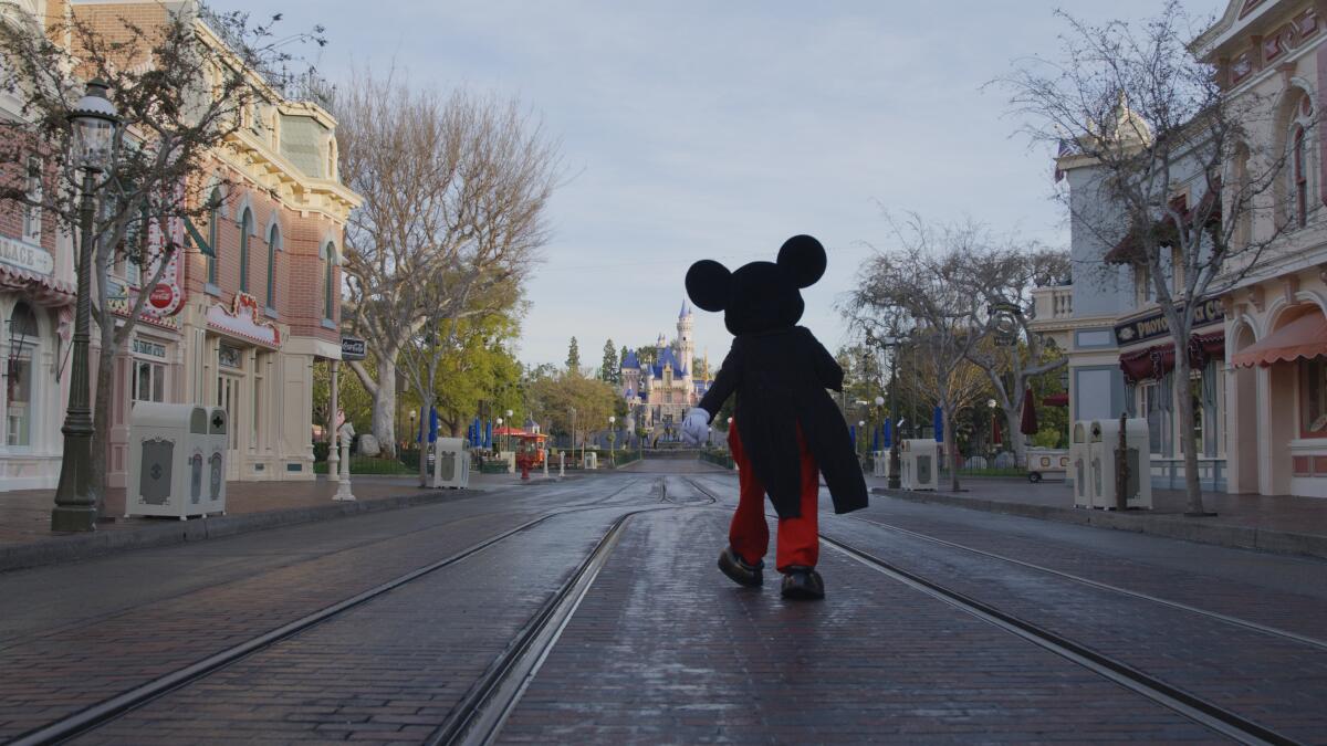 Von hinten ist ein Mickey-Mouse-Maskottchen zu sehen, das die Straße entlang geht