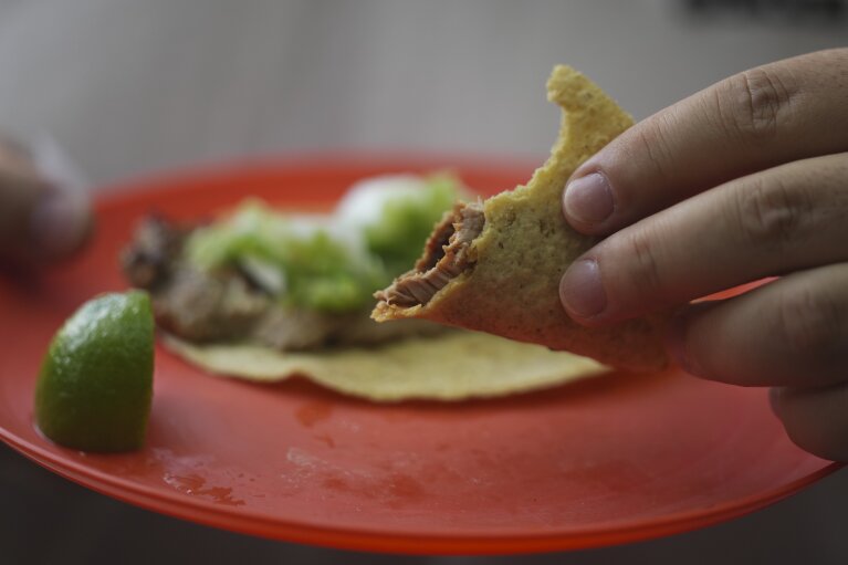 Ein Kunde hält seinen teilweise aufgegessenen Taco am Taco-Stand Tacos El Califa de León in Mexiko-Stadt, Mittwoch, 15. Mai 2024. Tacos El Califa de León ist der erste Taco-Stand überhaupt, der vom französischen Restaurantführer einen Michelin-Stern erhalten hat.  (AP Photo/Fernando Llano)